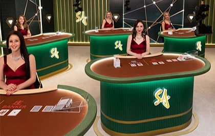 Live casino setting featuring five dealers in red dresses at green and brown gaming tables, with cards and chips visible.